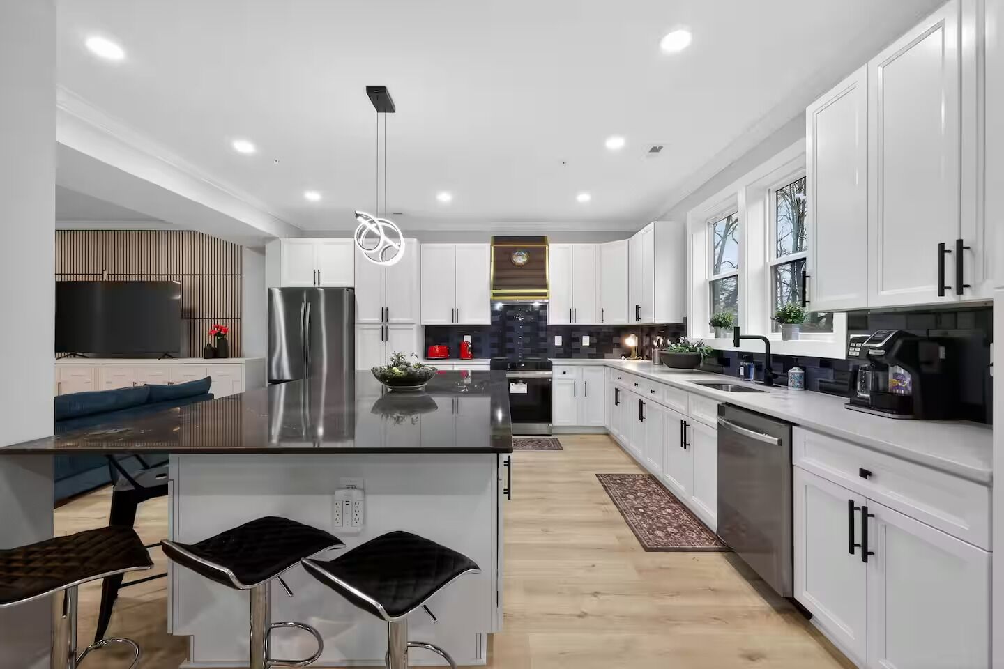 A modern kitchen with white cabinets, a central island, stainless steel appliances, and a dining area with bar stools.