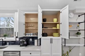 A modern kitchen with open cabinets, a coffee machine, and a window view. - Beautiful 5-bedroom house in welcoming Fort Washington (Fort Washington)