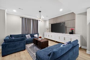 A modern living room with a sectional sofa, a coffee table, and a flat-screen TV mounted on a white cabinet. - Beautiful 5-bedroom house in welcoming Fort Washington (Fort Washington)