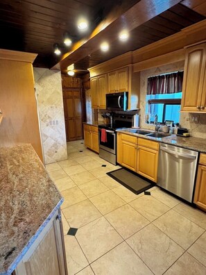 A kitchen with wooden cabinets, a granite countertop, a stainless steel dishwasher, and a microwave. - The Mossy Gambrel on Lake Huntley- fish, ski, swim, kayak and relax by fire pit! (Lake Placid)