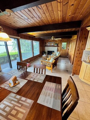 A wooden interior with a dining area, seating, and a fireplace. - The Mossy Gambrel on Lake Huntley- fish, ski, swim, kayak and relax by fire pit! (Lake Placid)