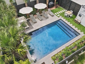 Ein rechteckiger Pool mit einer umlaufenden Liegefläche, Liegestühlen und Sonnenschirmen.