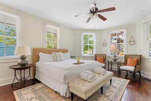 Quarto espaçoso com uma cama grande, um ventilador de teto e vista para o exterior pelas janelas.