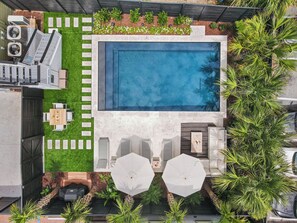 Vista aérea de um quintal com piscina, um pátio com mesa e cadeiras, e uma pequena área de jardim.