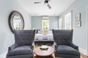 A bedroom with a bed, two armchairs, a round mirror, and a ceiling fan. - Mint Julep Residence @ Smalls Alley w/ Heated Saltwater Pool (Charleston)