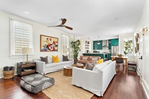 A modern living room with a white sofa, a coffee table, and a dining area with a kitchen in the background. - Mint Julep Residence @ Smalls Alley w/ Heated Saltwater Pool (Charleston)