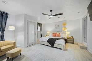 Un dormitorio con cama, mesitas de noche, ventilador de techo y ventana con cortinas.