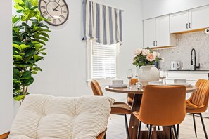 Un comedor moderno con una mesa redonda, sillas, un florero con flores y un reloj en la pared.