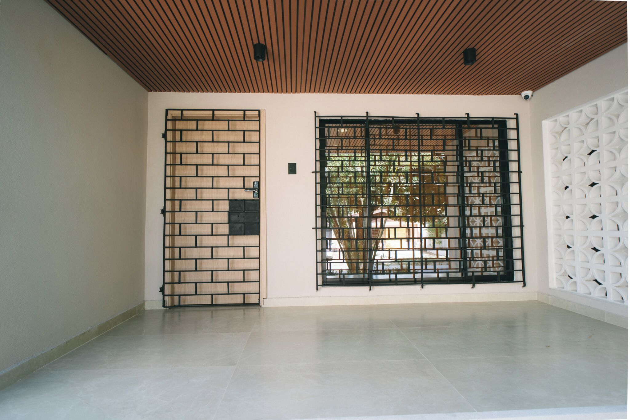 Una stanza con pavimento piastrellato, soffitto in legno, una parete divisoria in mattoni e un pannello decorativo bianco.