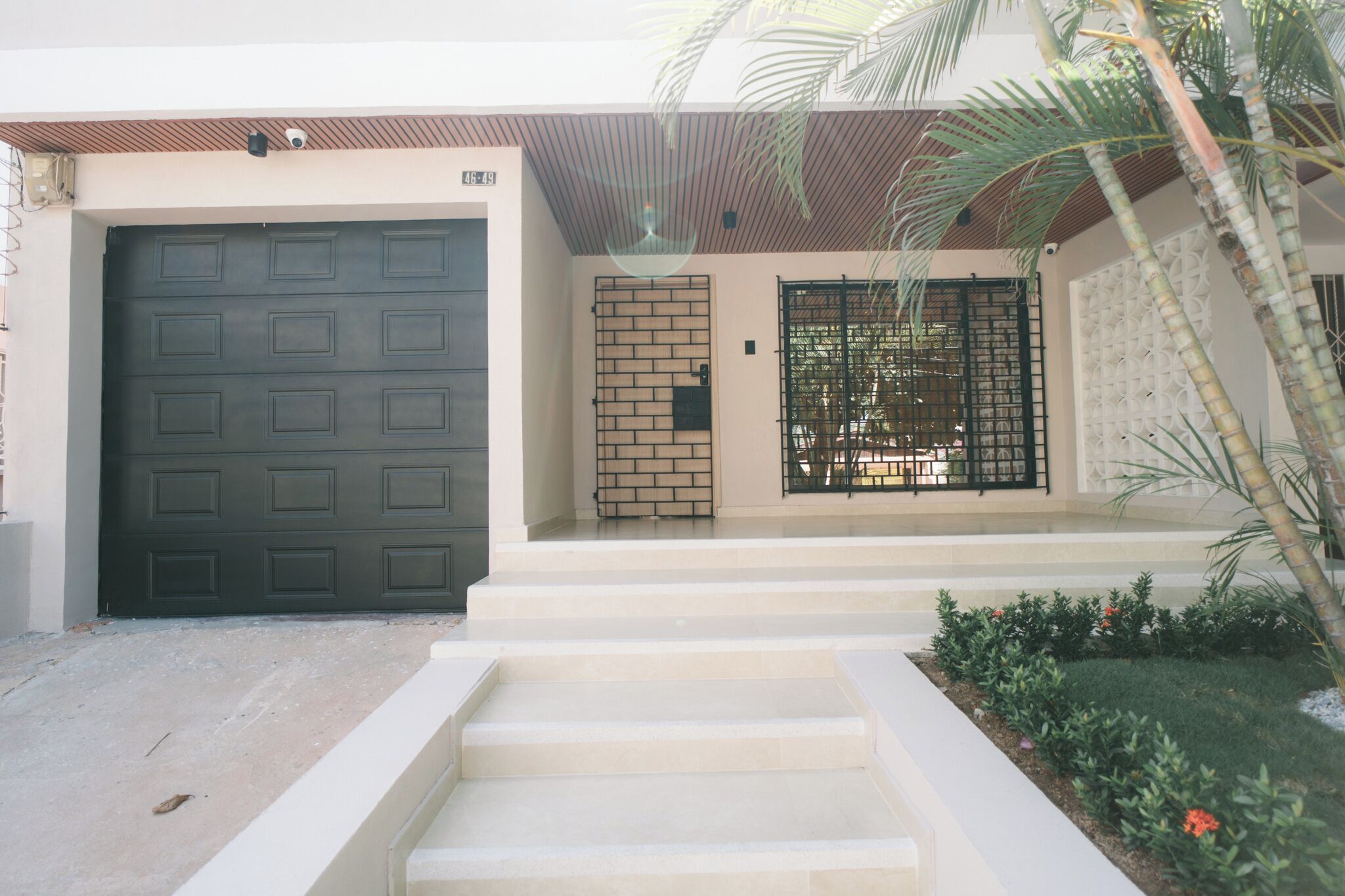 A residential entrance with a dark grey garage door, a brick wall gate, and a black metal gate.