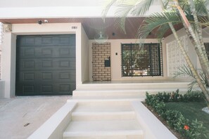 A residential entrance with a dark grey garage door, a brick wall gate, and a black metal gate. - Casa Obregón (Barranquilla)