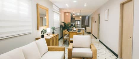 A hotel lobby with a reception desk, seating area with sofas and chairs, a dining table, and a kitchen in the background.