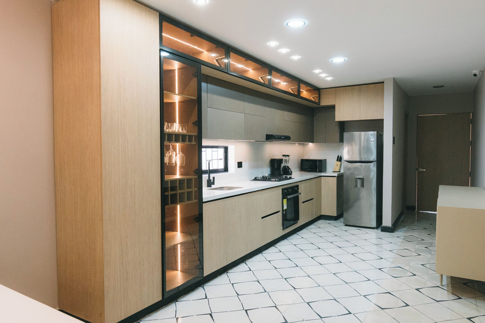 Une cuisine moderne dotée d’un four, d’un micro-ondes et d’un réfrigérateur encastrés, avec un revêtement en bois clair et un éclairage sous les meubles hauts.