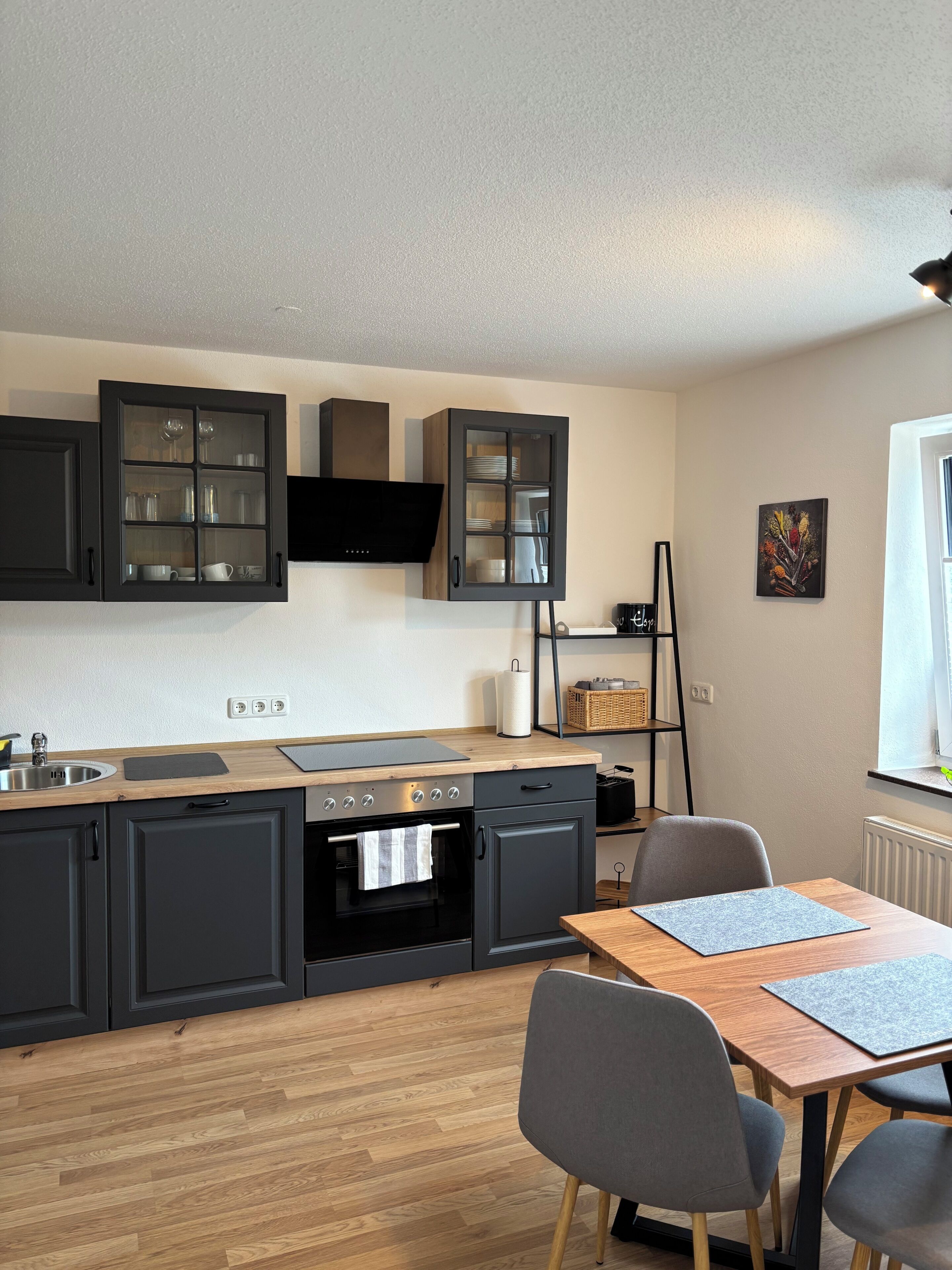 Une cuisine moderne avec des meubles de couleur sombre, un plan de travail en bois et un coin repas comprenant une table et des chaises.