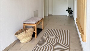 Un corridoio con una panca, un cesto di vimini, un tappeto decorato, mensole in legno, uno specchio e una porta con la scritta 'Private'.