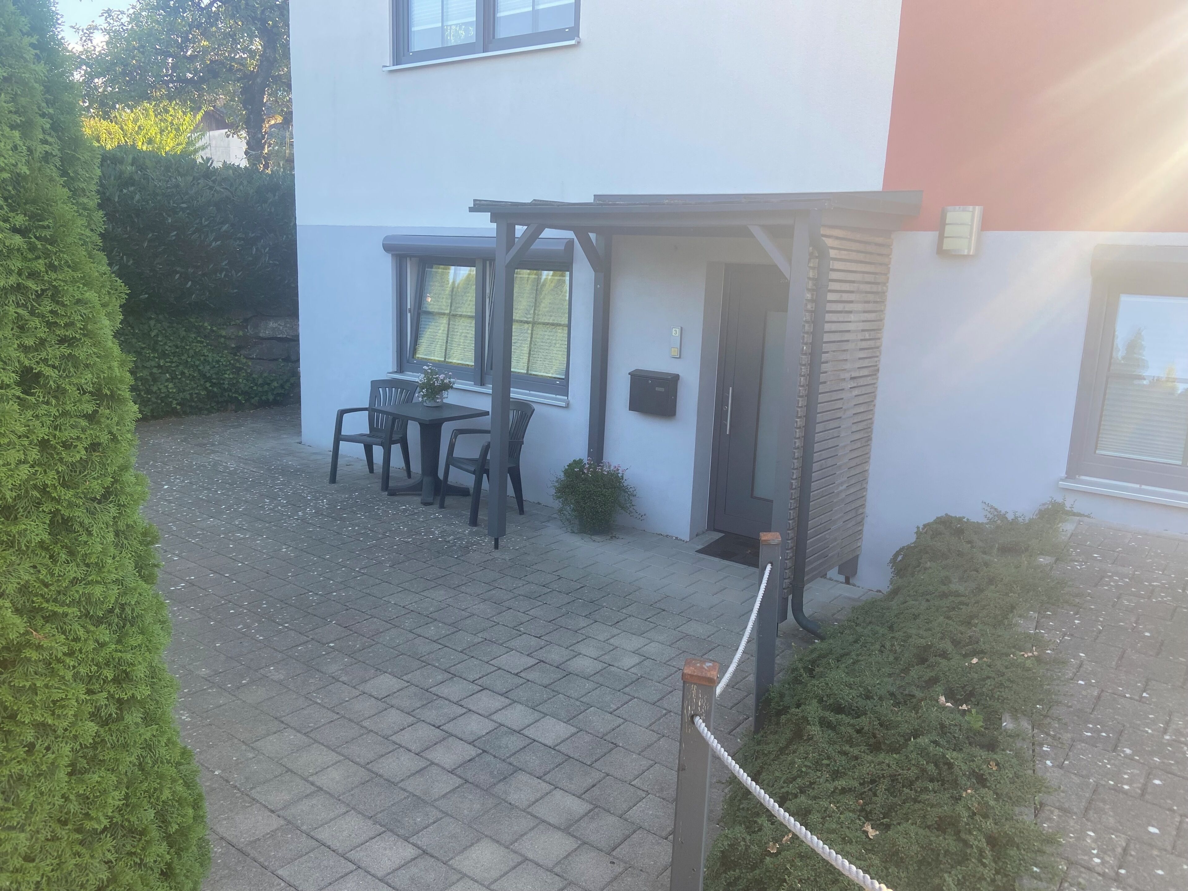 Une cour avec une table et des chaises, une porte et un petit espace jardin.