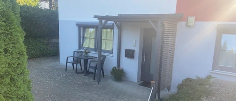 Un patio con una mesa, sillas, una puerta y un pequeño jardín.