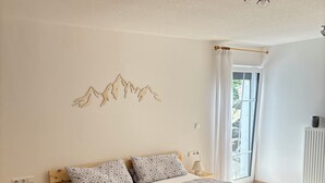 Una camera da letto con un letto di legno, biancheria a motivi, un punto luce a parete, una finestra con tende e un termosifone.