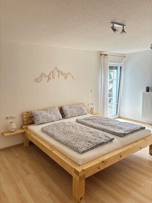Ein Schlafzimmer mit einem hölzernen Bett, gemusterten Betttextilien, einer Wandleuchte, einem Fenster mit Vorhängen und einer Heizung.