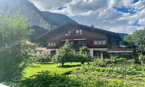 Eine zweistöckige Chalet mit Garten, umgeben von Bergen.