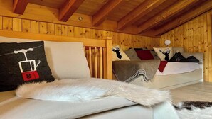 A cozy room with wooden walls and a sloped ceiling. There is a bed with a white blanket and a pillow with a ski lift design. - BEAUTIFUL 2-BEDROOM CHALET WITH PANORAMIC MOUNTAIN VIEWS (Lauterbrunnen)