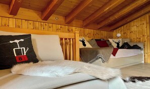 Ein gemütliches Zimmer mit Holzwänden und einer schrägen Decke. Ein Bett mit weißer Decke und einem Kopfkissen mit einem Skilift-Motiv.