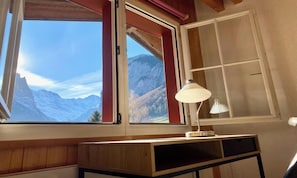 A room with a desk, a lamp, and a window with a mountain view. - BEAUTIFUL 2-BEDROOM CHALET WITH PANORAMIC MOUNTAIN VIEWS (Lauterbrunnen)