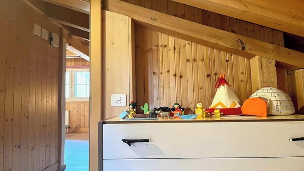A wooden interior with a white dresser, a window, and a shelf with various toys and a teepee. - BEAUTIFUL 2-BEDROOM CHALET WITH PANORAMIC MOUNTAIN VIEWS (Lauterbrunnen)