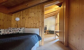 A wooden interior with a bed, a white wall, and a door leading to another room. - BEAUTIFUL 2-BEDROOM CHALET WITH PANORAMIC MOUNTAIN VIEWS (Lauterbrunnen)