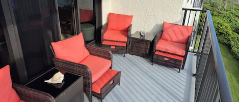 Un balcon doté de meubles en osier et de coussins rouges, offrant une vue sur une plage et une végétation luxuriante.