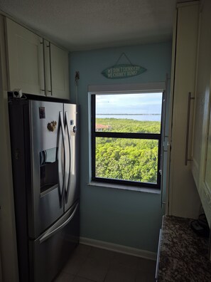 Eine Küche mit einem Edelstahl-Kühlschrank, einem Fenster mit Blick auf Grünflächen und ein Gewässer, sowie ein Schild an der Wand.