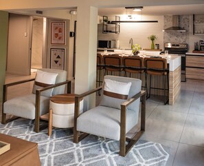 Een moderne keuken met een centraal eiland, barstoelen en een eethoek met stoelen.