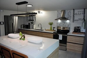 A modern kitchen with a central island, stainless steel appliances, and a marble backsplash. - Modern hidden retreat with chef’s kitchen, spa bath, pergola, bar & solar-power. (Boquerón)