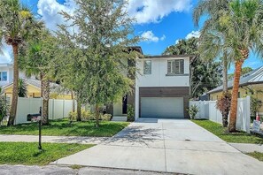 A two-story residential house with a garage, surrounded by a white fence, palm trees, and a clear sky. - 4-bedroom Sarasota Pool/Spa Retreat. Near Downtown & Beaches (Sarasota)