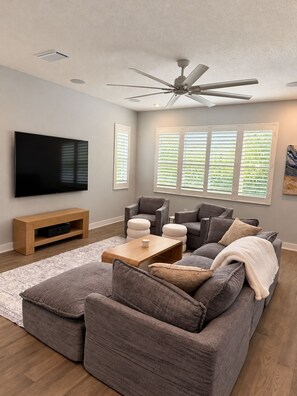 A modern living room with a flat-screen TV, grey sofas, a wooden coffee table, and a ceiling fan. - 4-bedroom Sarasota Pool/Spa Retreat. Near Downtown & Beaches (Sarasota)