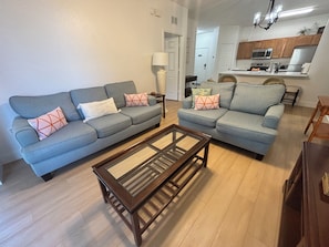 A living room with two sofas, a coffee table, and a kitchen in the background. - NEW!  2 bed condo, near Disney, Margaritaville.  Pool, free water park, AC, gym. (Kissimmee)