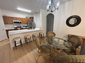 Una cucina moderna con mobili in legno, un'isola centrale con sgabelli da bar, un tavolo da pranzo in vetro e un lampadario.