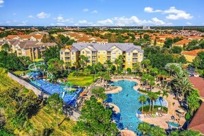 A resort with a large swimming pool, multiple buildings, and a well-maintained landscape. - NEW!  2 bed condo, near Disney, Margaritaville.  Pool, free water park, AC, gym. (Kissimmee)