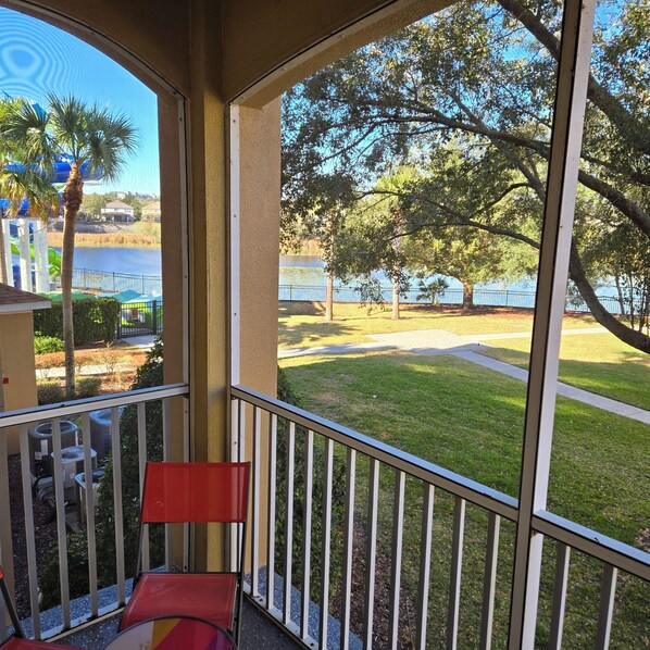 A balcony with a view of a lake, trees, and a distant building.