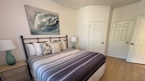 Ein Schlafzimmer mit Bett, Nachttisch, Lampe, einem Bild und einer Tür.