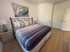 A bedroom with a bed, a nightstand, a lamp, a painting, and a door.