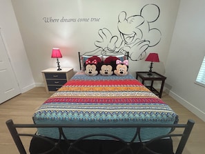 A bedroom with a bed, two nightstands, a wall with a Mickey Mouse mural, and a bedspread with a pattern. - NEW!  2 bed condo, near Disney, Margaritaville.  Pool, free water park, AC, gym. (Kissimmee)