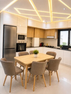 A modern kitchen with a built-in oven, a refrigerator, and a dining area with a table and chairs.