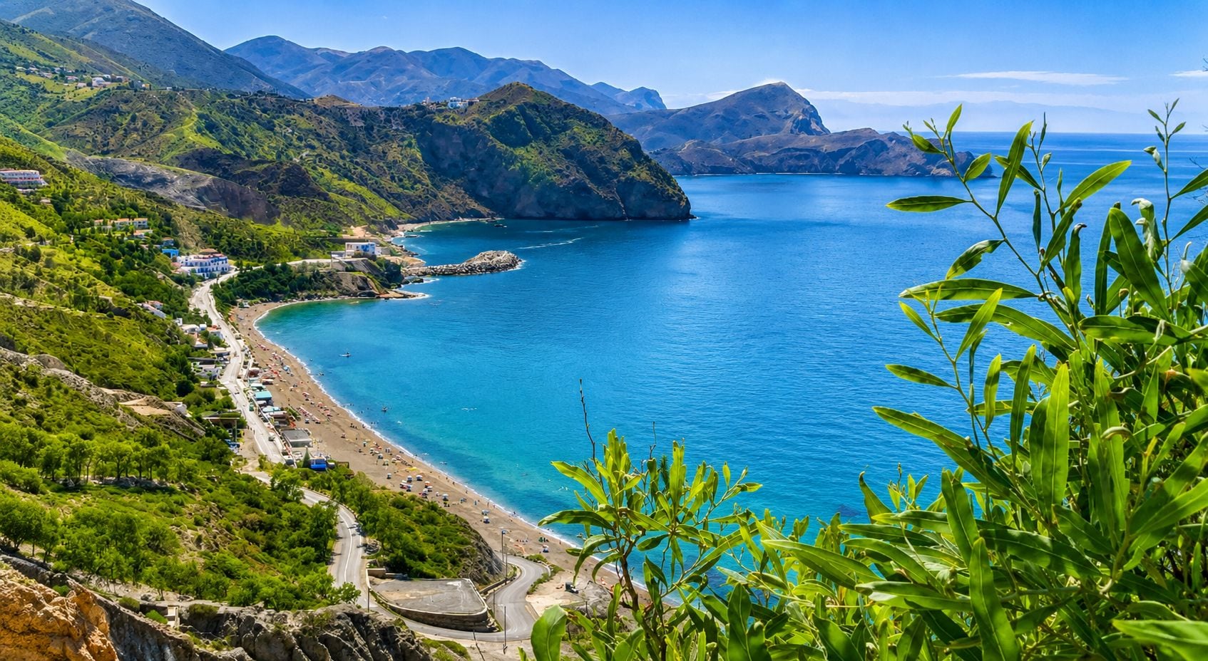 A coastal landscape with a beach, a road, and buildings.