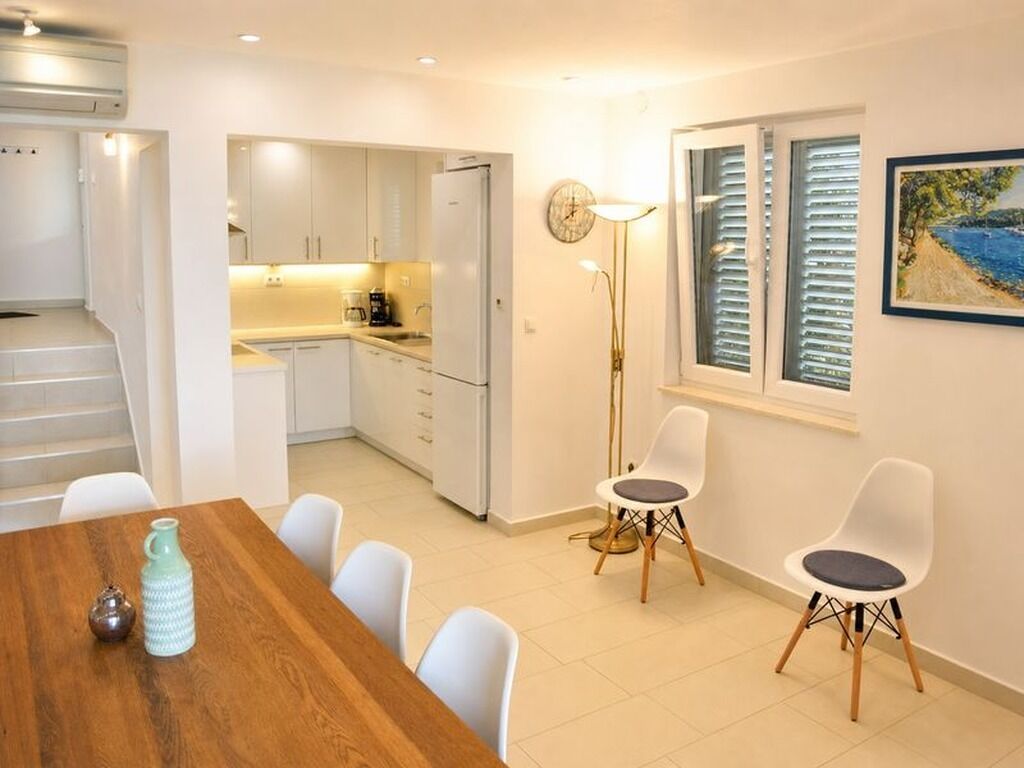 A modern kitchen with white cabinets, a dining area with a wooden table and white chairs, and a painting on the wall.