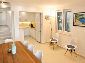 A modern kitchen with white cabinets, a dining area with a wooden table and white chairs, and a painting on the wall. - Unique villa right on the beach with its own dock. Completely renovated, Zadar (Bibinje)