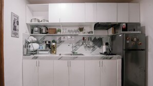 Eine kompakte Küche mit weißen Schränken, einem Edelstahlkühlschrank und einer Mikrowelle obenauf.