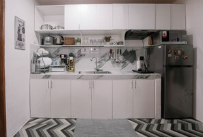 Una cucina compatta con mobili bianchi, un frigorifero in acciaio inossidabile e un microonde sopra.