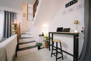 A modern apartment with a staircase, a desk with two laptops, a small stool, and a potted plant.