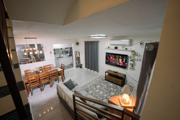 A modern living room with a dining area, a TV, and a staircase leading to another level.